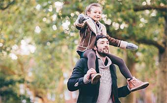 child on shoulders of dad walking through leaves